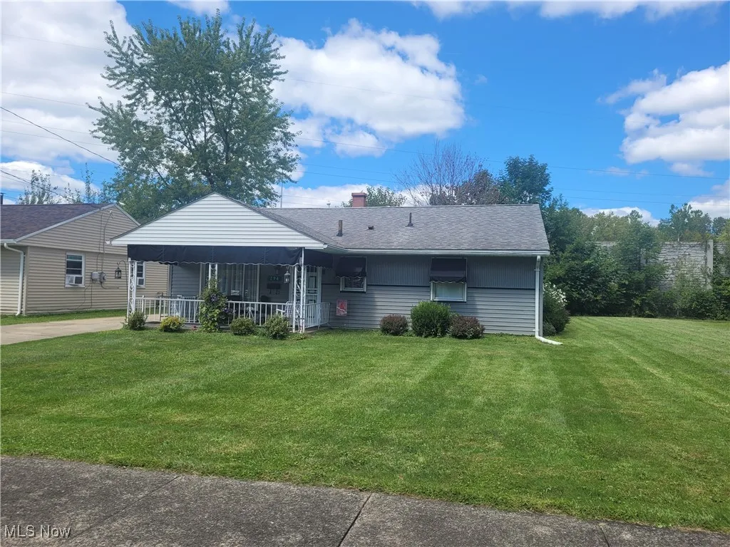 View of front of property featuring a front yard, a chimney, roof with shingles, and covered porch