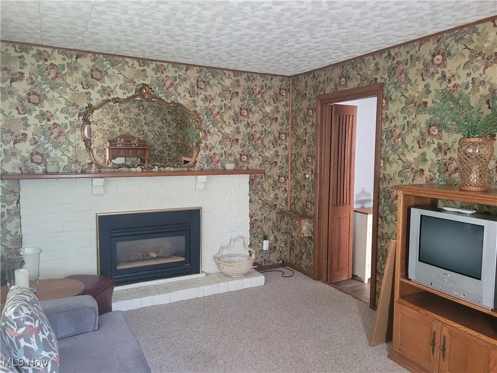 Living area with carpet flooring, a brick fireplace, and wallpapered walls