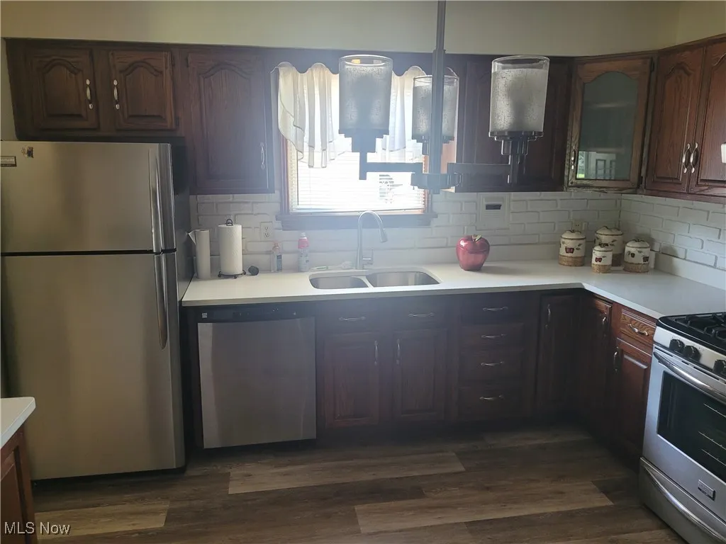 Kitchen with appliances with stainless steel finishes, light countertops, backsplash, and dark wood-style floors