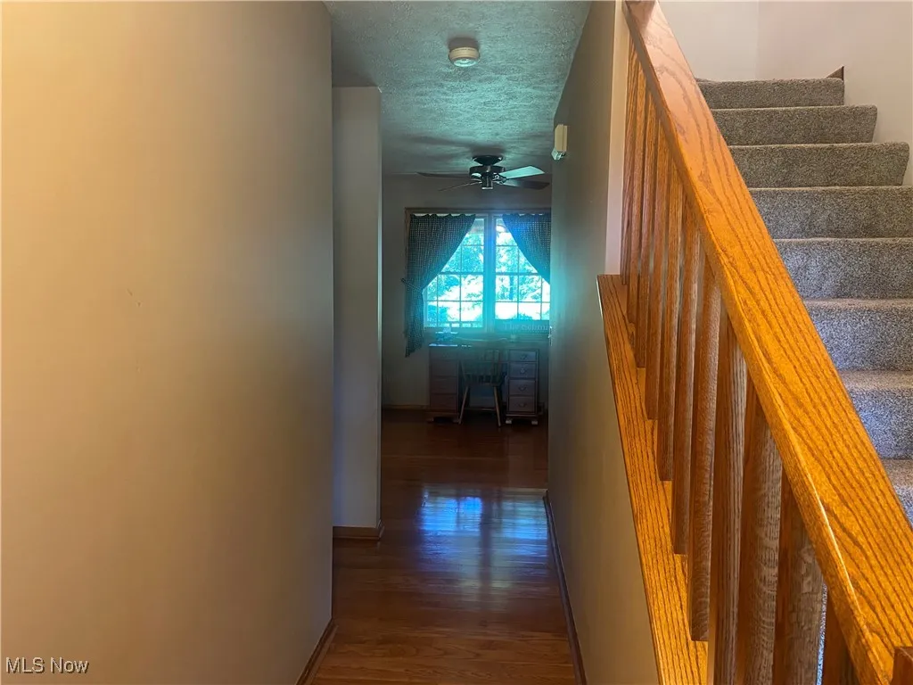 Hall with wood finished floors, a textured ceiling, and stairway
