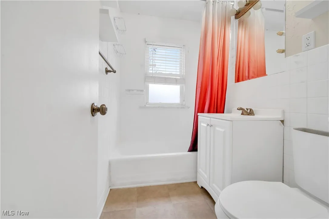 Full bathroom featuring vanity, shower / bathtub combination with curtain, tile patterned floors, toilet, and tile walls