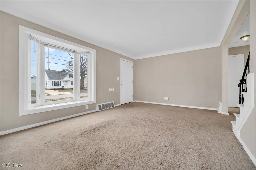 Unfurnished living room featuring visible vents, baseboards, carpet flooring, and stairway