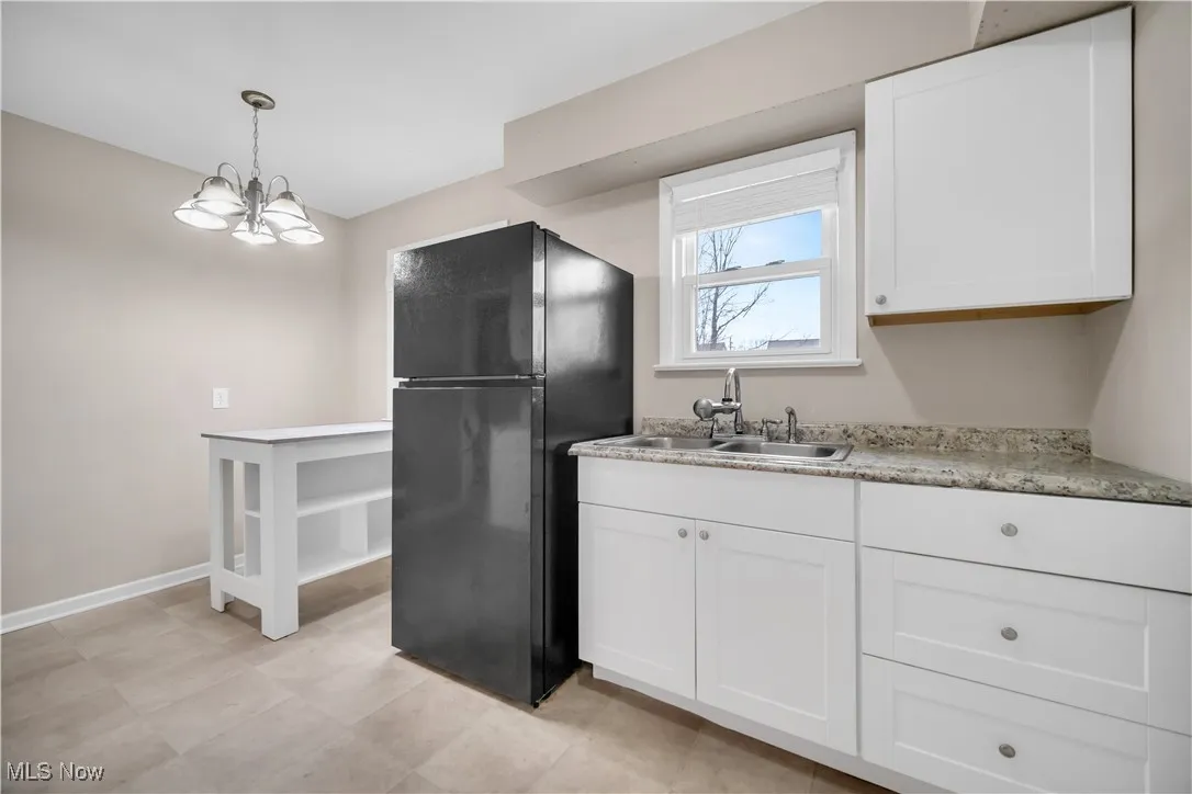 Kitchen with pendant lighting, a sink, freestanding refrigerator, white cabinets, and baseboards