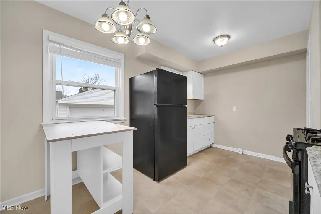 Kitchen with baseboards, a notable chandelier, black appliances, and white cabinets