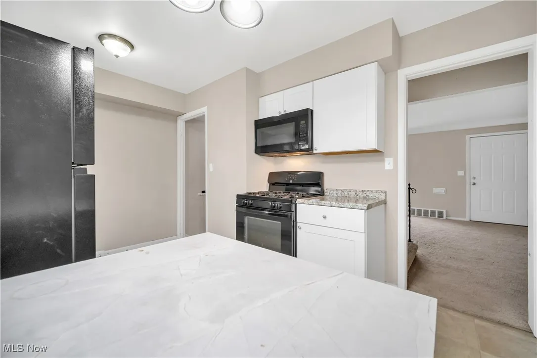Kitchen featuring light carpet, visible vents, white cabinetry, and black appliances