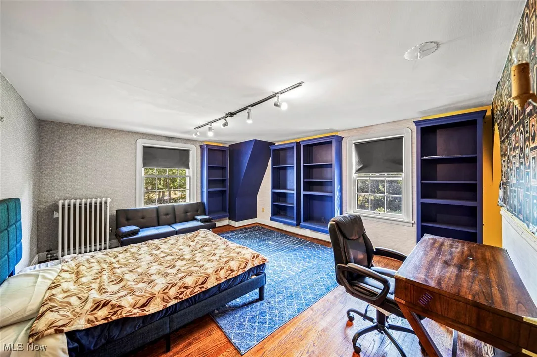 Bedroom with wood finished floors, radiator heating unit, rail lighting, a desk, and wallpapered walls
