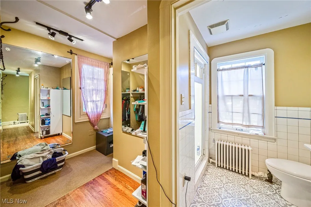 Bathroom with light wood finished floors, radiator, a shower stall, track lighting, and tile walls