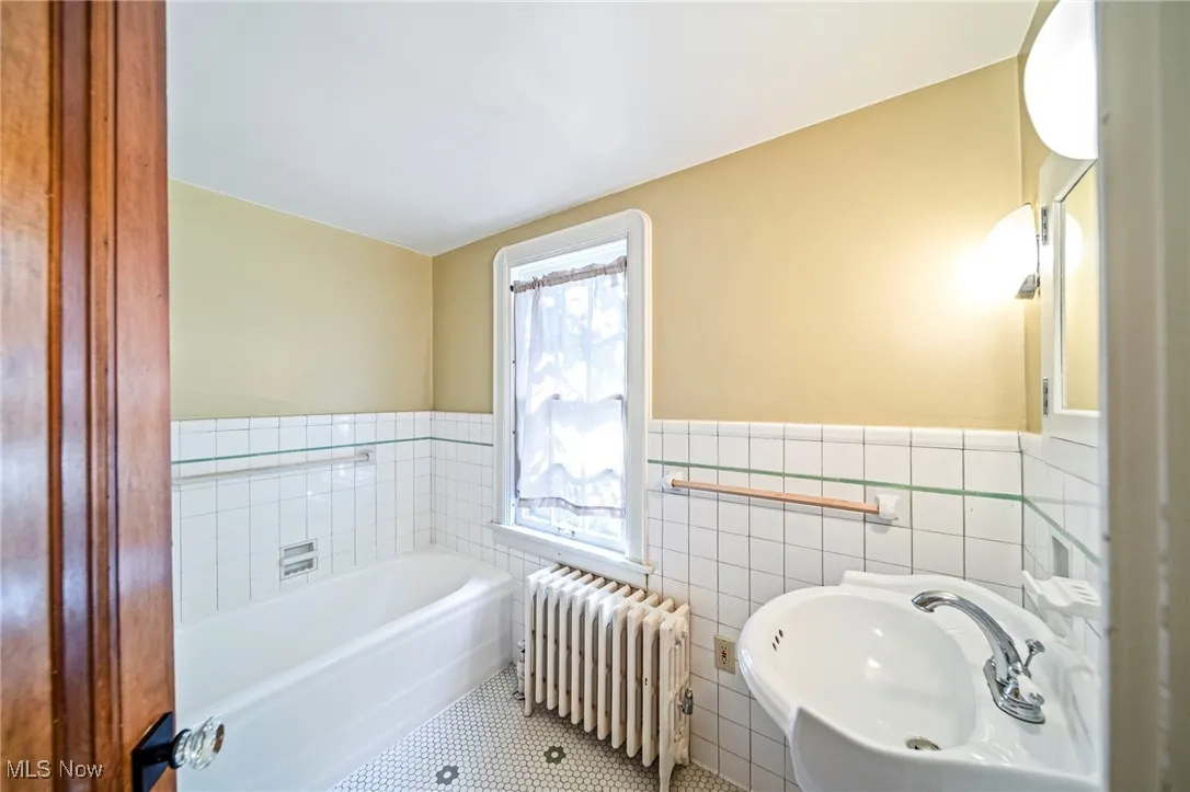Full bathroom featuring tile walls, radiator heating unit, a garden tub, wainscoting, and tile patterned flooring