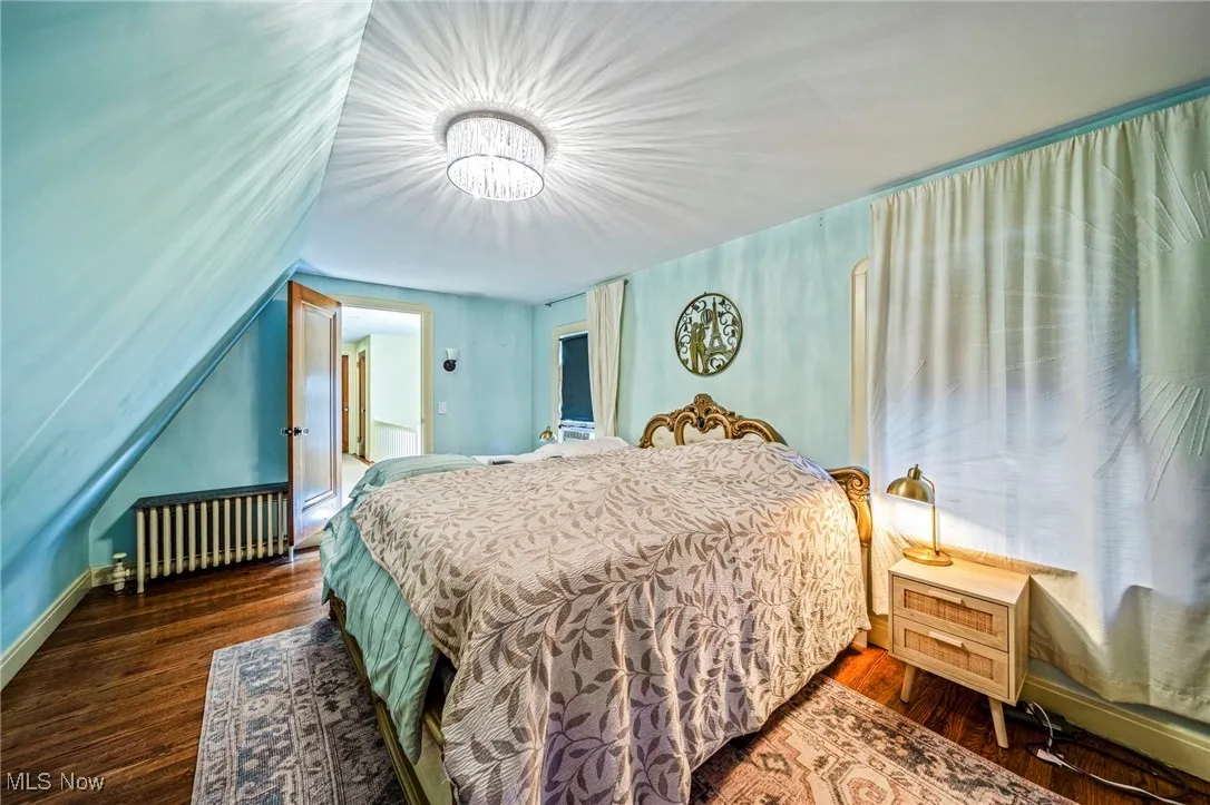 Bedroom featuring dark wood-style flooring, radiator heating unit, and a chandelier