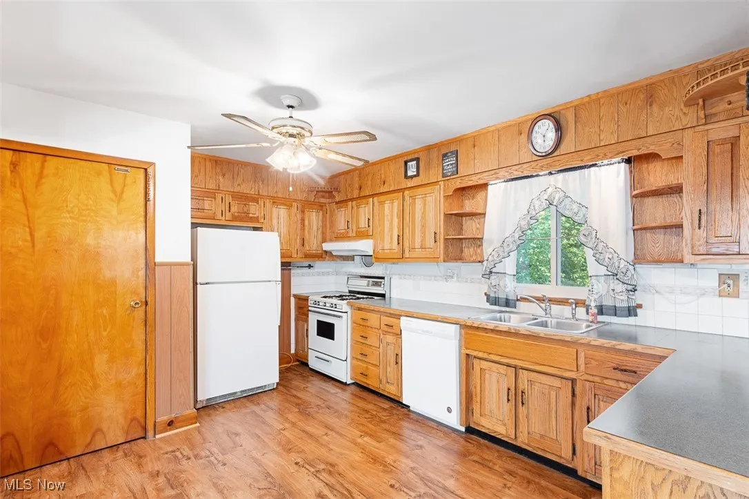 Kitchen with white appliances, light wood-type flooring, open shelves, a ceiling fan, and wooden walls