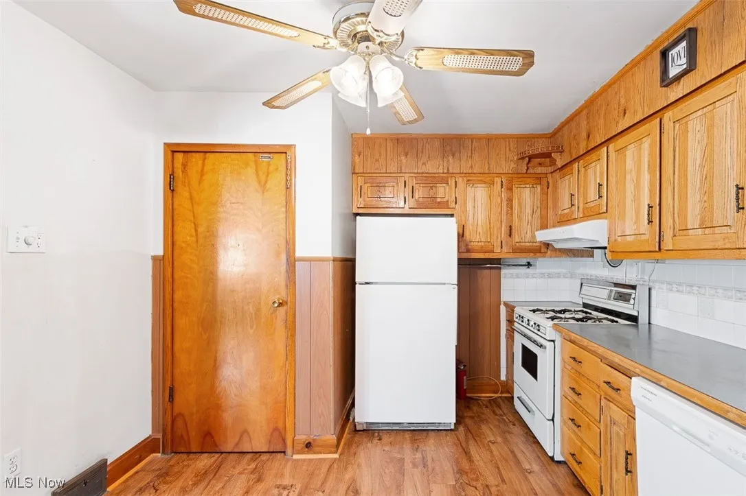 Kitchen with white appliances, light wood-style floors, light countertops, under cabinet range hood, and a ceiling fan