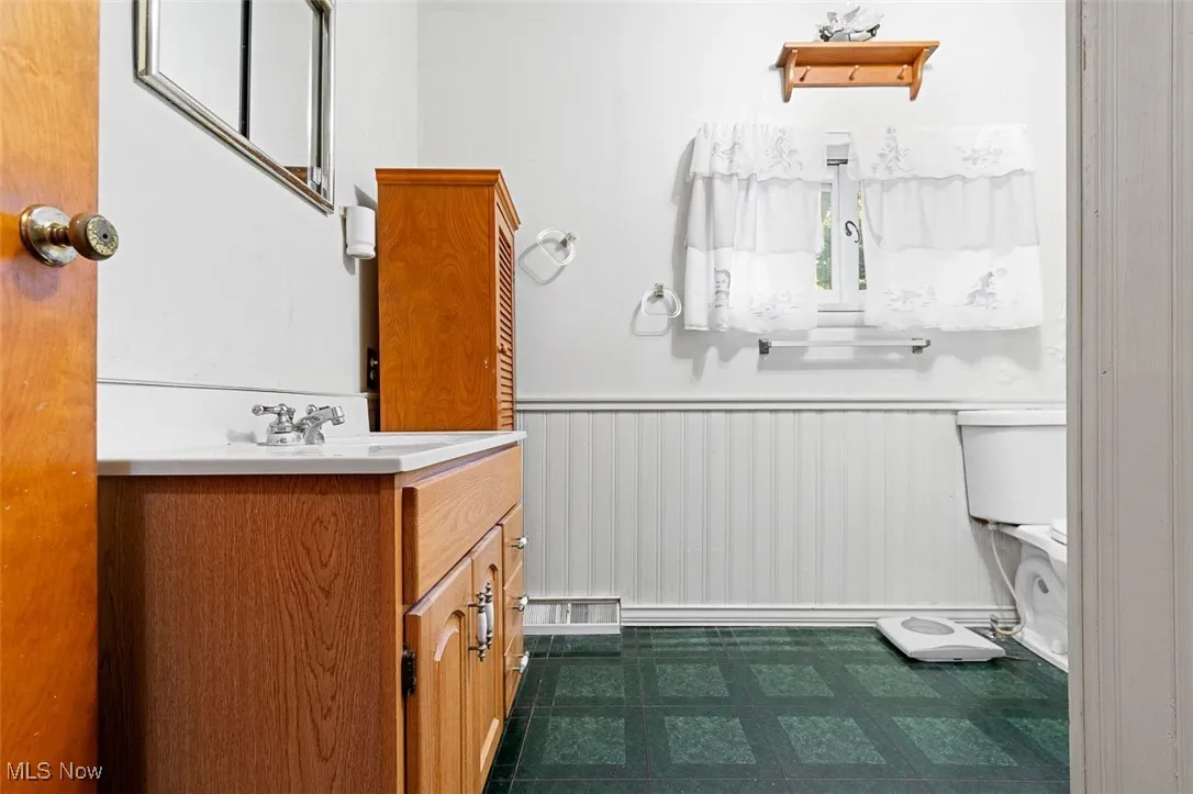 Half bathroom featuring vanity, a wainscoted wall, and dark flooring