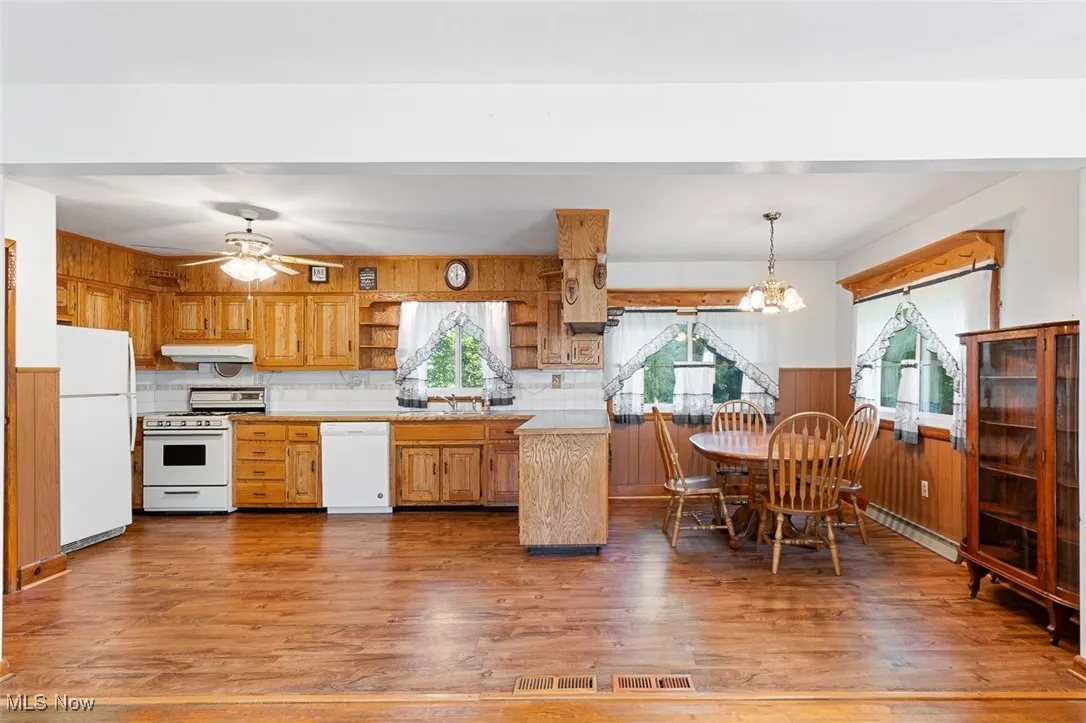 Kitchen featuring light countertops, wood walls, white appliances, light wood finished floors, and brown cabinets