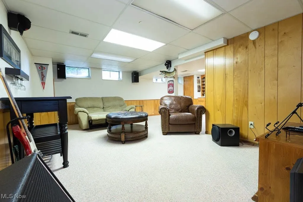 Living area with wood walls, a drop ceiling, and carpet flooring