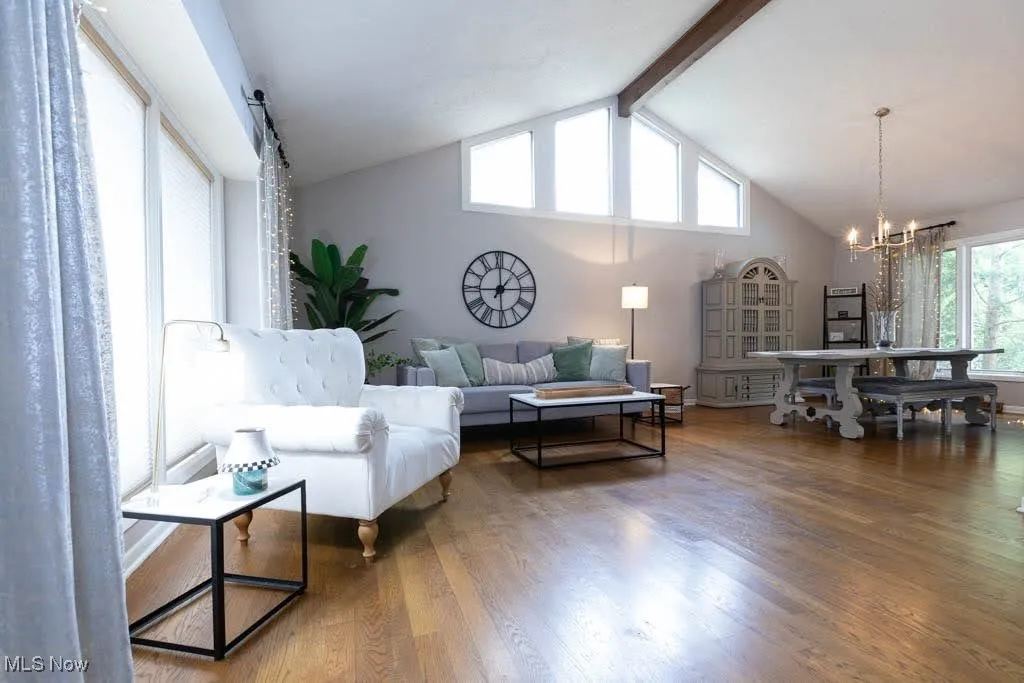 Living room with high vaulted ceiling, wood finished floors, beamed ceiling, and a chandelier