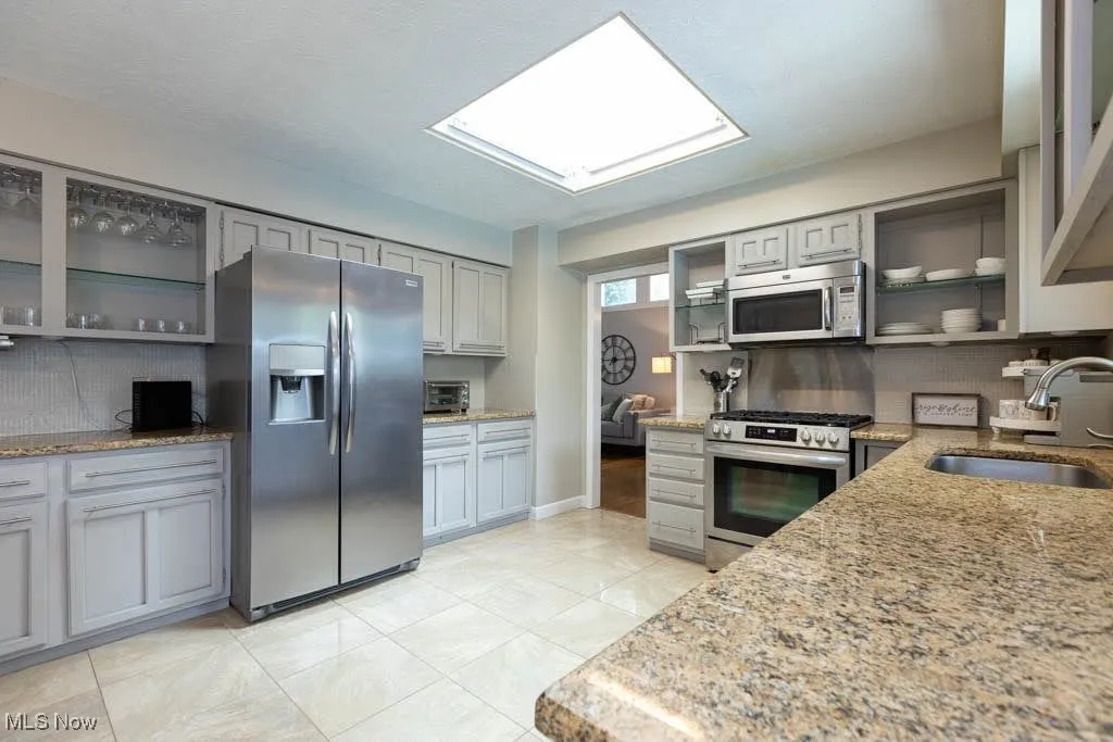 Kitchen with glass insert cabinets, gray cabinets, decorative backsplash, and appliances with stainless steel finishes