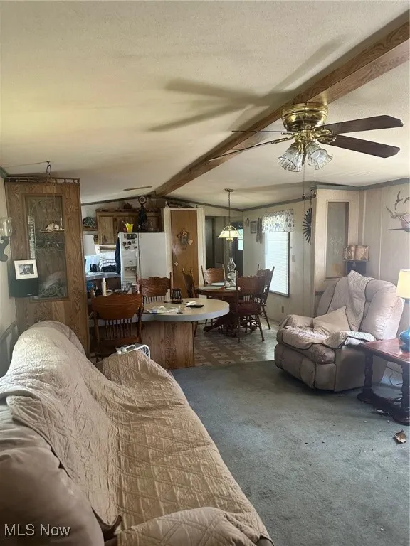 Carpeted living area featuring beamed ceiling, ceiling fan, and a textured ceiling