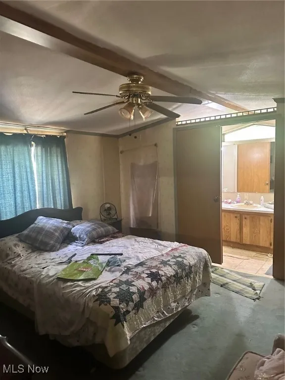 Carpeted bedroom with beam ceiling, ceiling fan, and connected bathroom