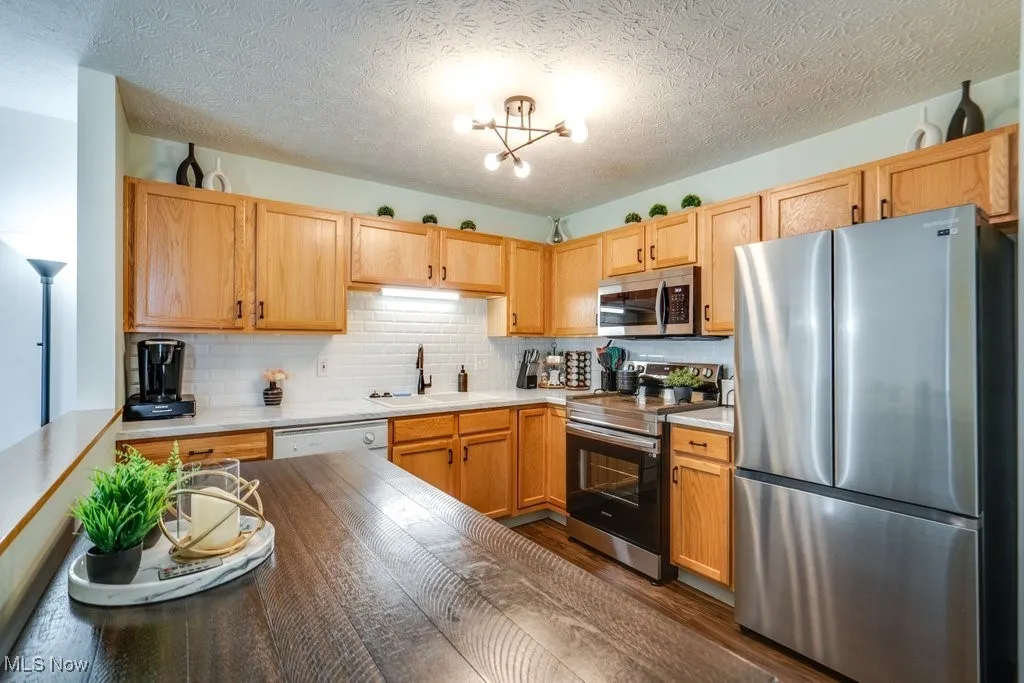 Kitchen with stainless steel appliances, dark wood-style flooring, backsplash, a textured ceiling, and a chandelier