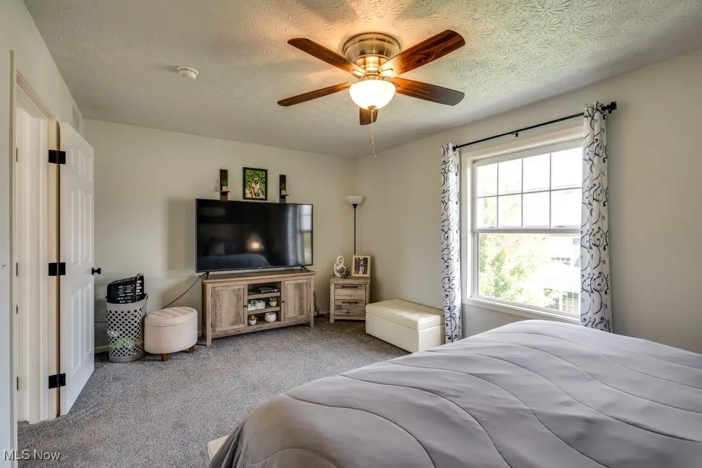 Bedroom with carpet floors, ceiling fan, and a textured ceiling