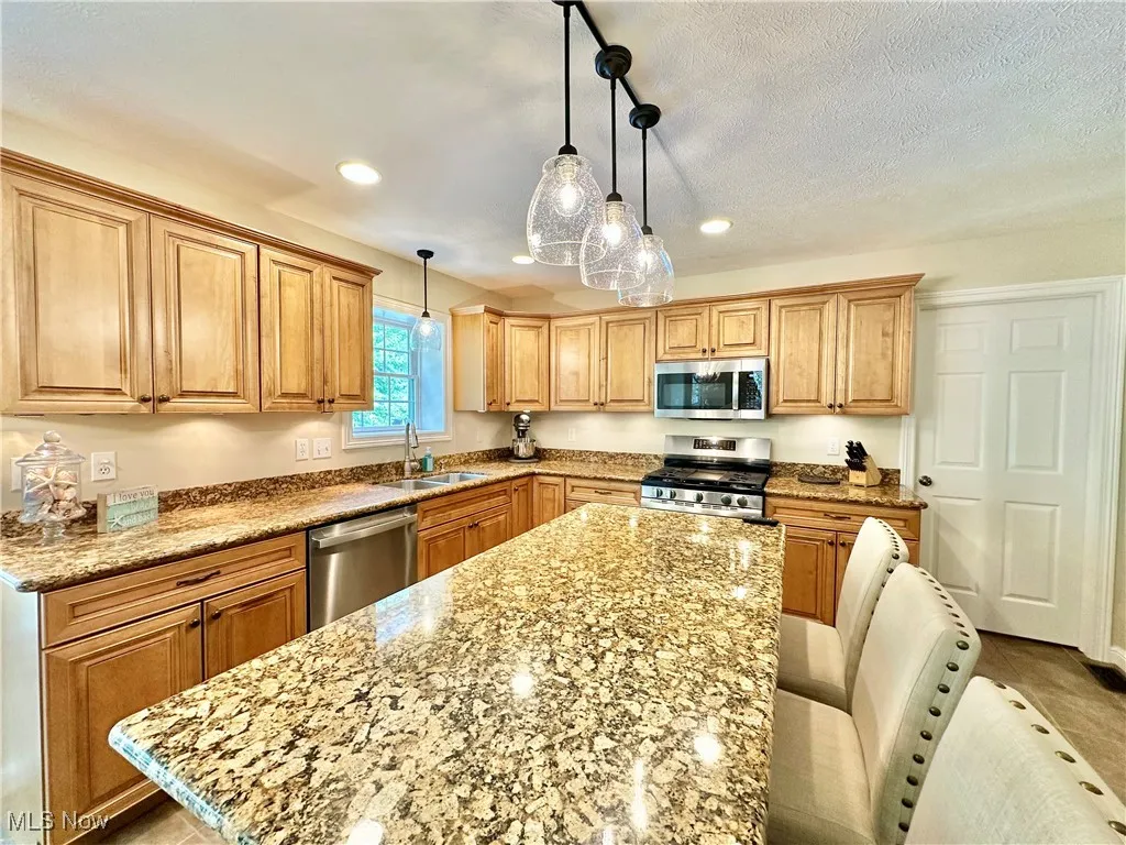 Kitchen featuring hanging light fixtures, appliances with stainless steel finishes, light stone counters, recessed lighting, and a center island