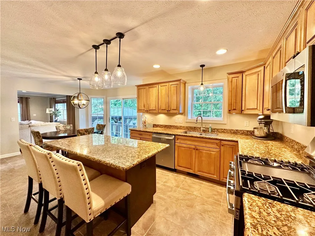 Kitchen with stainless steel appliances, hanging light fixtures, a breakfast bar area, a kitchen island, and light stone countertops