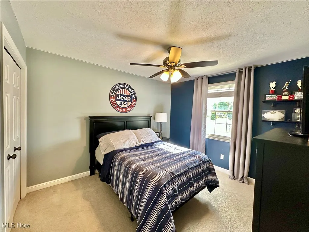 Bedroom with a closet, light carpet, a textured ceiling, and a ceiling fan
