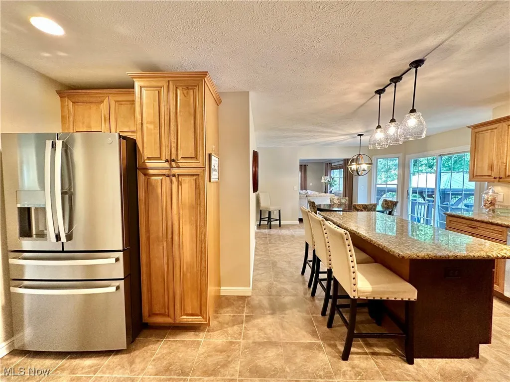 Kitchen featuring stainless steel refrigerator with ice dispenser, a kitchen breakfast bar, a center island, pendant lighting, and light stone counters