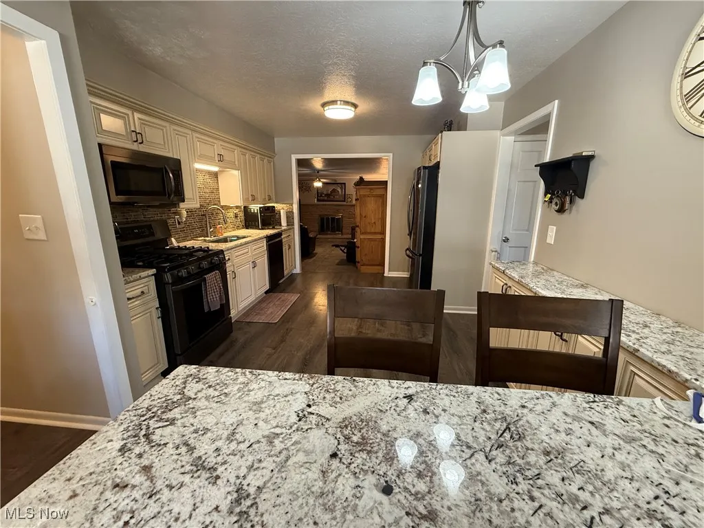 Kitchen featuring appliances with stainless steel finishes, decorative backsplash, a textured ceiling, decorative light fixtures, and light stone counters