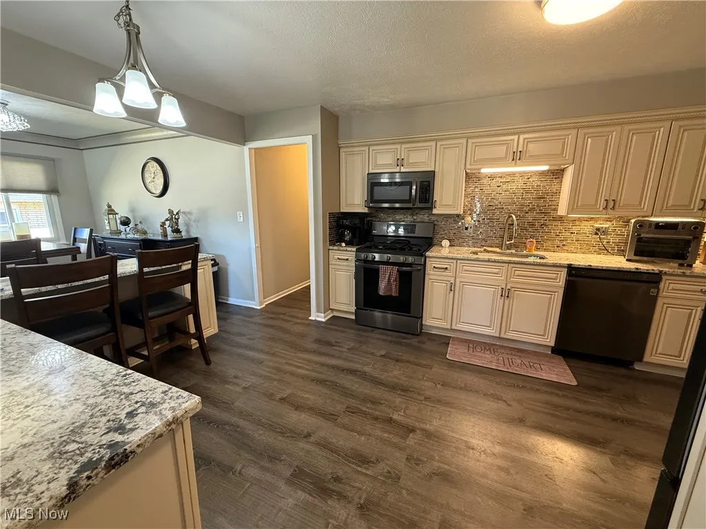 Kitchen featuring stainless steel appliances, cream cabinets, decorative backsplash, decorative light fixtures, and a textured ceiling