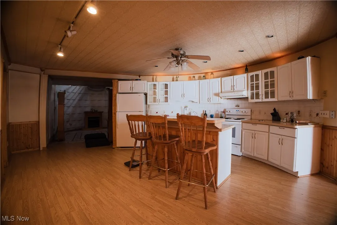 Kitchen with glass insert cabinets, a kitchen bar, light countertops, light wood-style floors, and white appliances