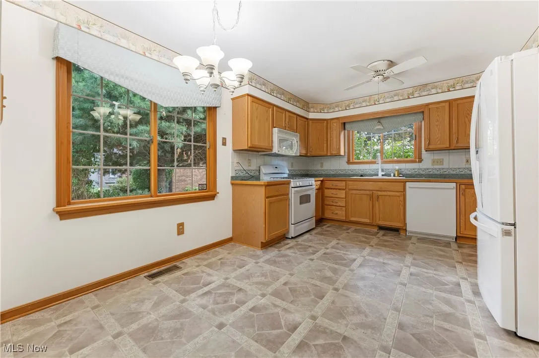 Kitchen featuring white appliances, a chandelier, pendant lighting, and tasteful backsplash