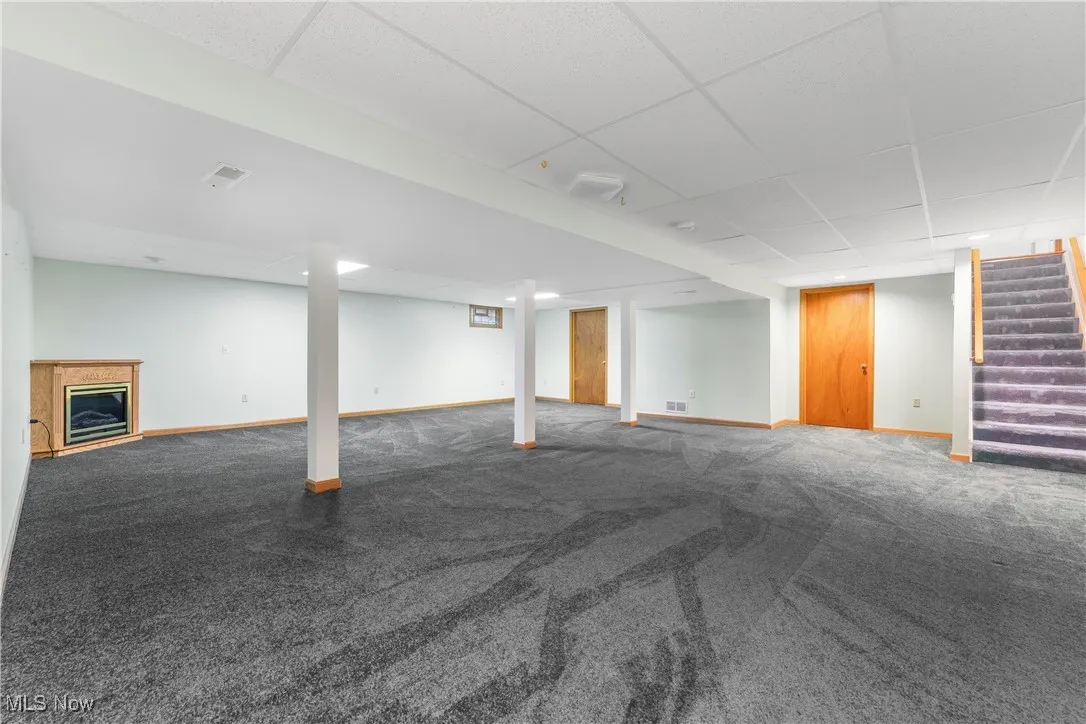 Finished below grade area featuring a paneled ceiling, a glass covered fireplace, carpet flooring, and stairs