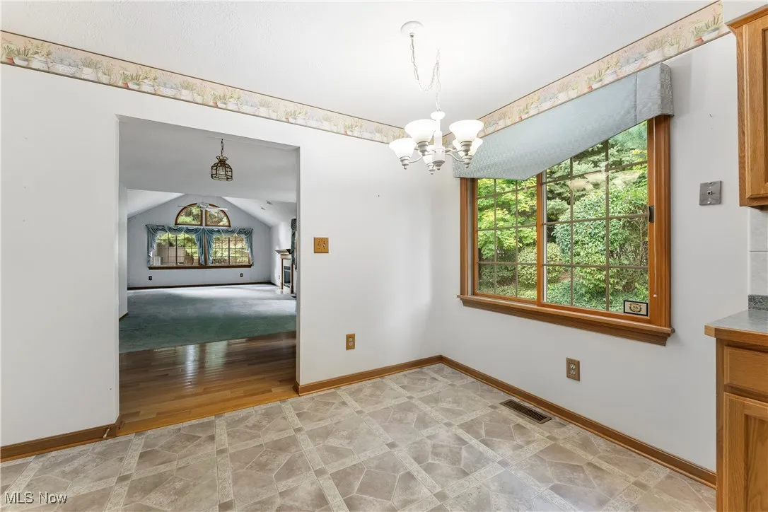 Unfurnished dining area with a chandelier, vaulted ceiling, and light wood-style floors