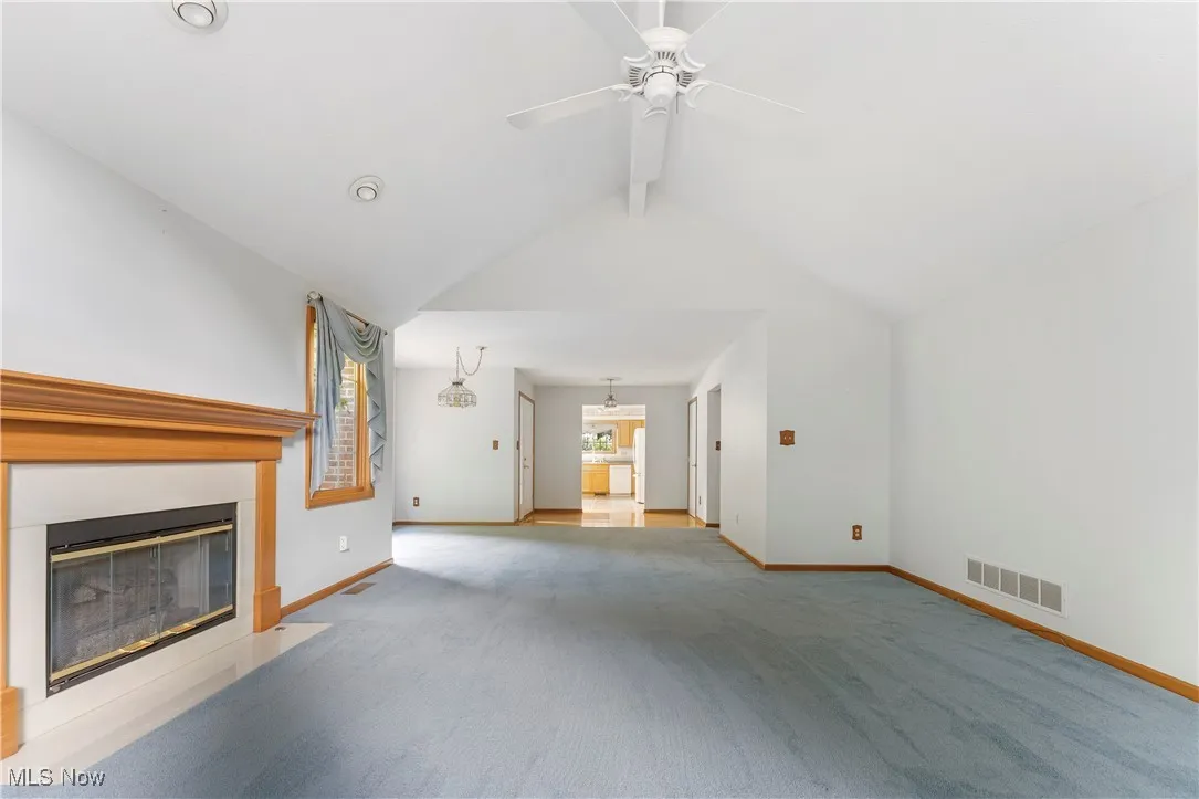 Unfurnished living room with light colored carpet, a glass covered fireplace, and a ceiling fan