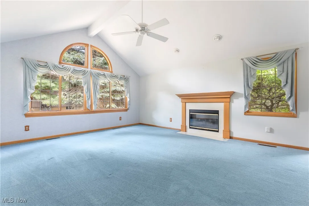Unfurnished living room featuring beamed ceiling, carpet floors, a fireplace with flush hearth, high vaulted ceiling, and ceiling fan