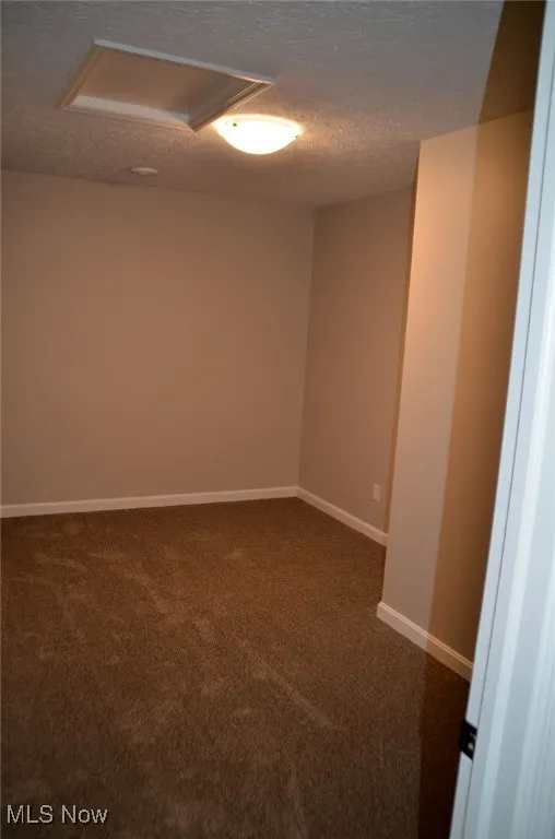 Spare room featuring dark colored carpet and a textured ceiling
