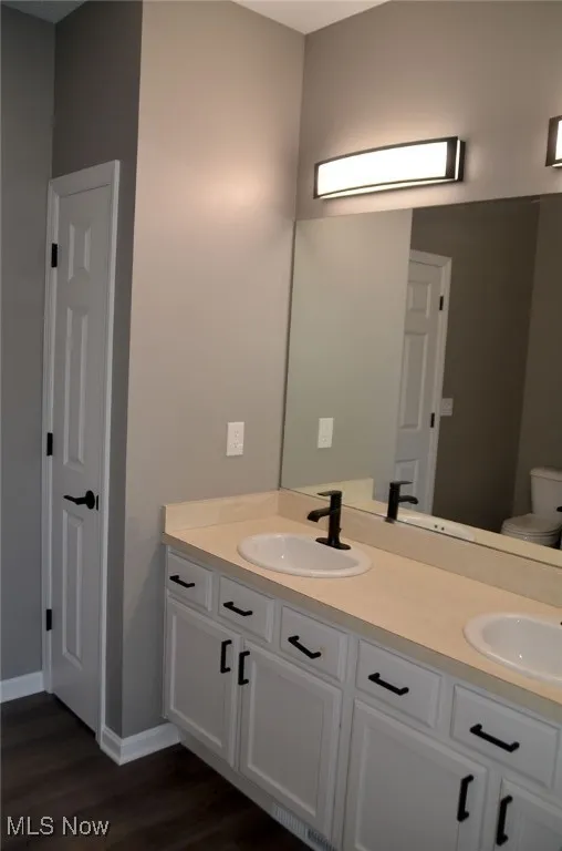 Full bath with double vanity and dark wood-type flooring