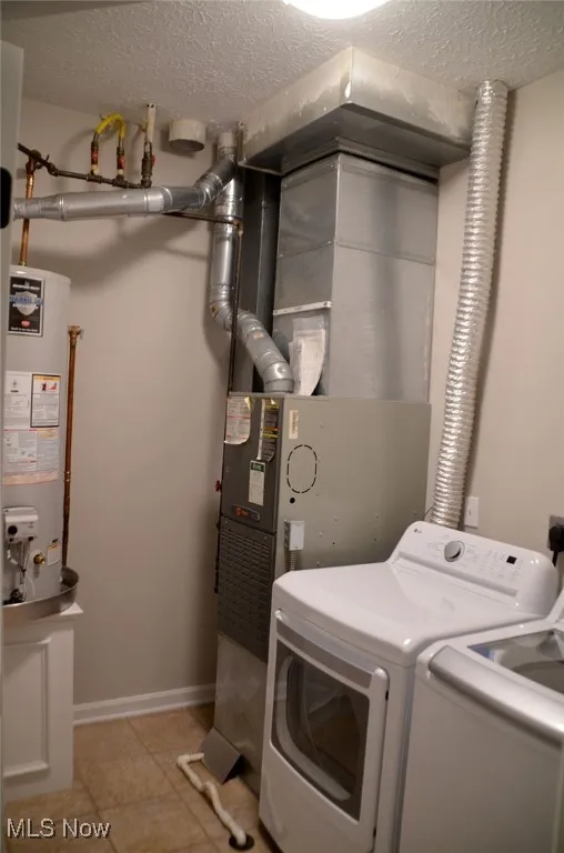 Laundry area featuring a textured ceiling, gas water heater, heating unit, light tile patterned floors, and independent washer and dryer