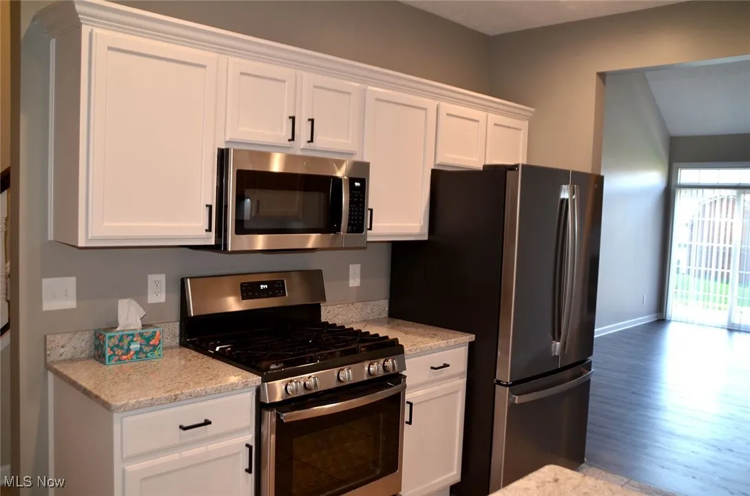 Kitchen with appliances with stainless steel finishes, white cabinetry, and light stone counters
