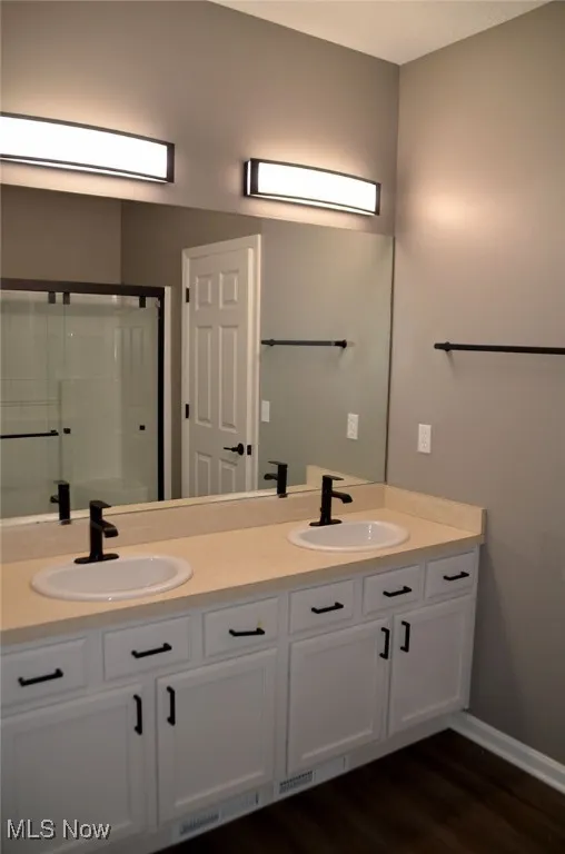 Bathroom with double vanity, dark wood-style floors, and a shower stall