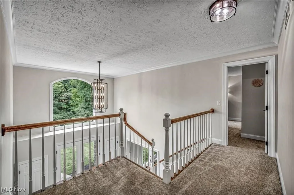 Hall featuring an upstairs landing, carpet, a textured ceiling, a chandelier, and ornamental molding
