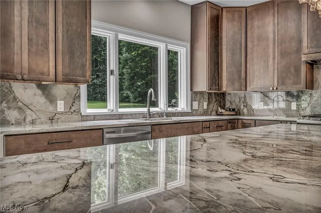 Kitchen featuring light stone counters, decorative backsplash, dishwasher, and dark brown cabinets