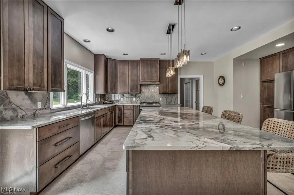 Kitchen featuring a breakfast bar area, light stone countertops, dark brown cabinets, a spacious island, and pendant lighting