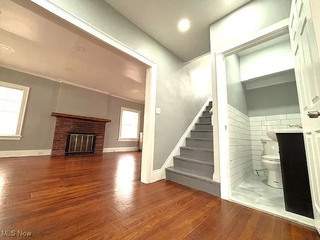 Staircase with wood finished floors, a brick fireplace, crown molding, and recessed lighting