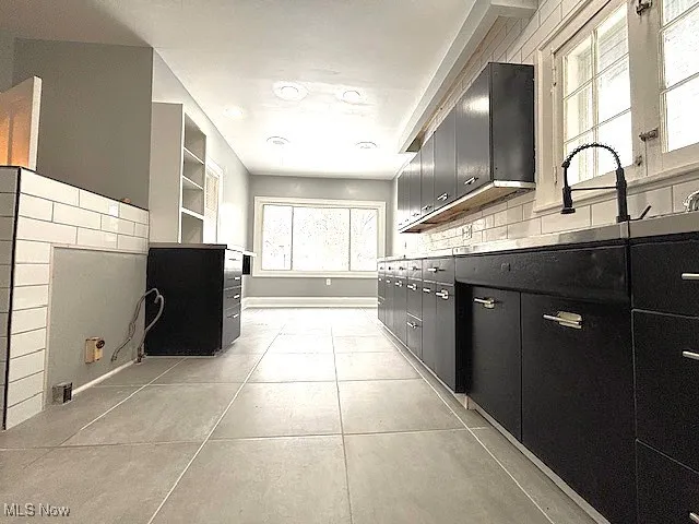 Kitchen featuring dark cabinets, light tile patterned floors, decorative backsplash, open shelves, and light countertops