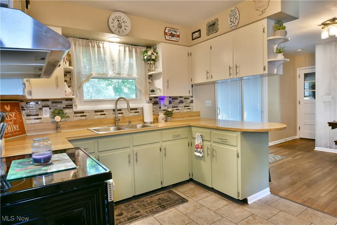 Kitchen featuring open shelves, green cabinets, a peninsula, extractor fan, and black range with electric stovetop