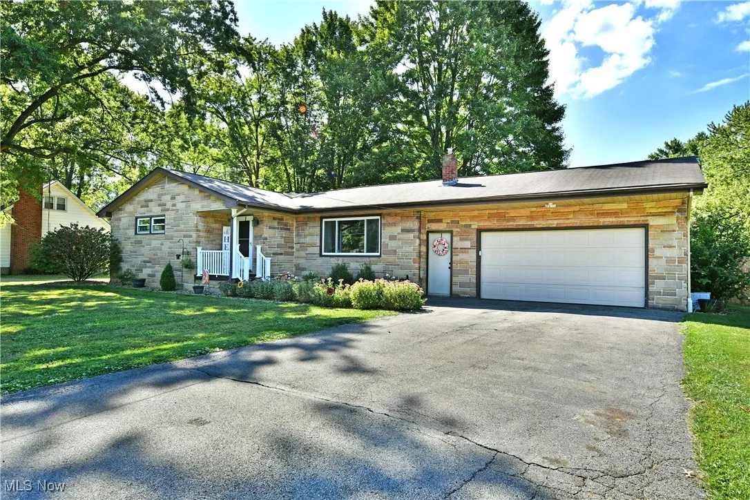 Ranch-style house with stone siding, asphalt driveway, a chimney, a front yard, and a garage