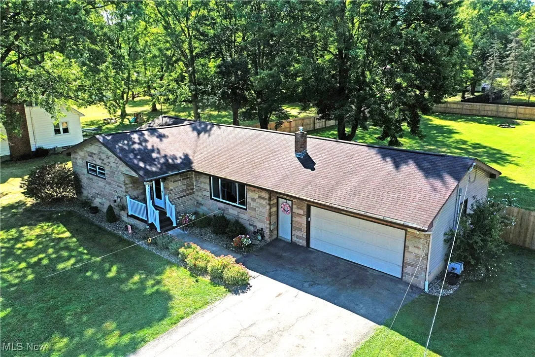 Ranch-style house featuring driveway, a garage, stone siding, a chimney, and roof with shingles
