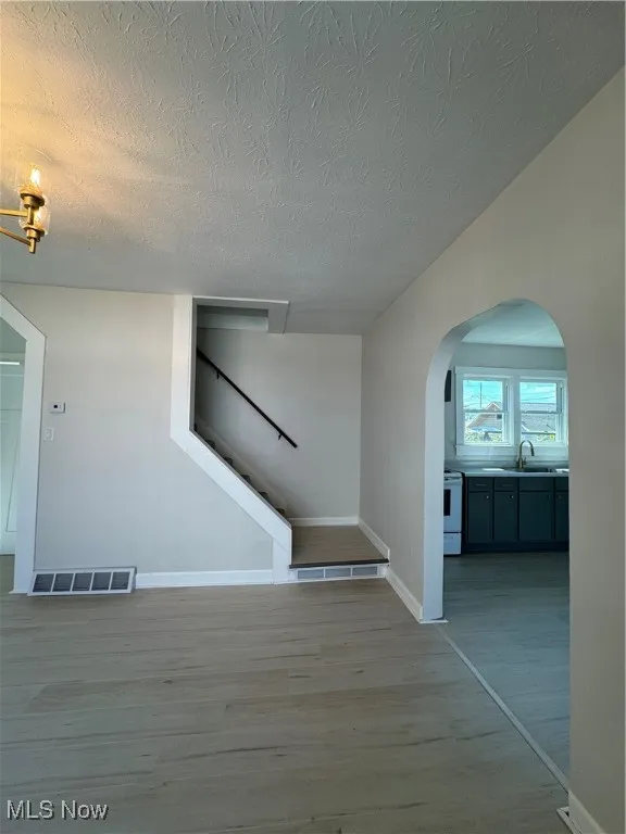 Unfurnished living room featuring arched walkways, light wood-type flooring, a textured ceiling, and stairs